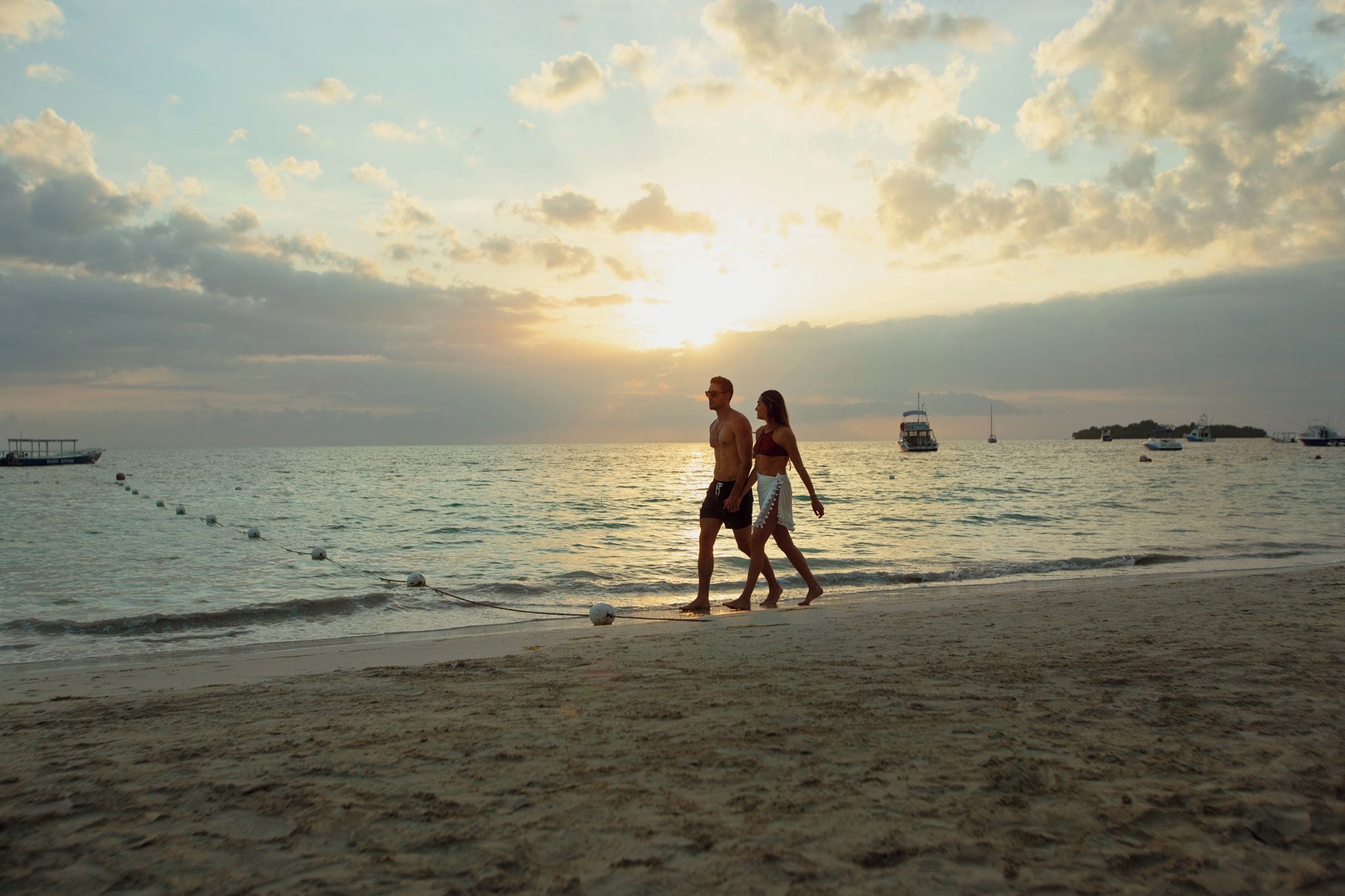 Une scène de plage avec un coucher de soleil, un bateau et une personne qui se promène.
