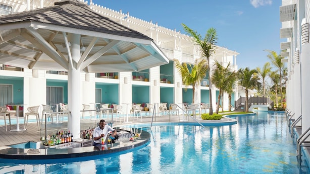 A poolside bar area with a bartender, lounge chairs, and a pool. - Azul Beach Resort Negril By Karisma (Negril)