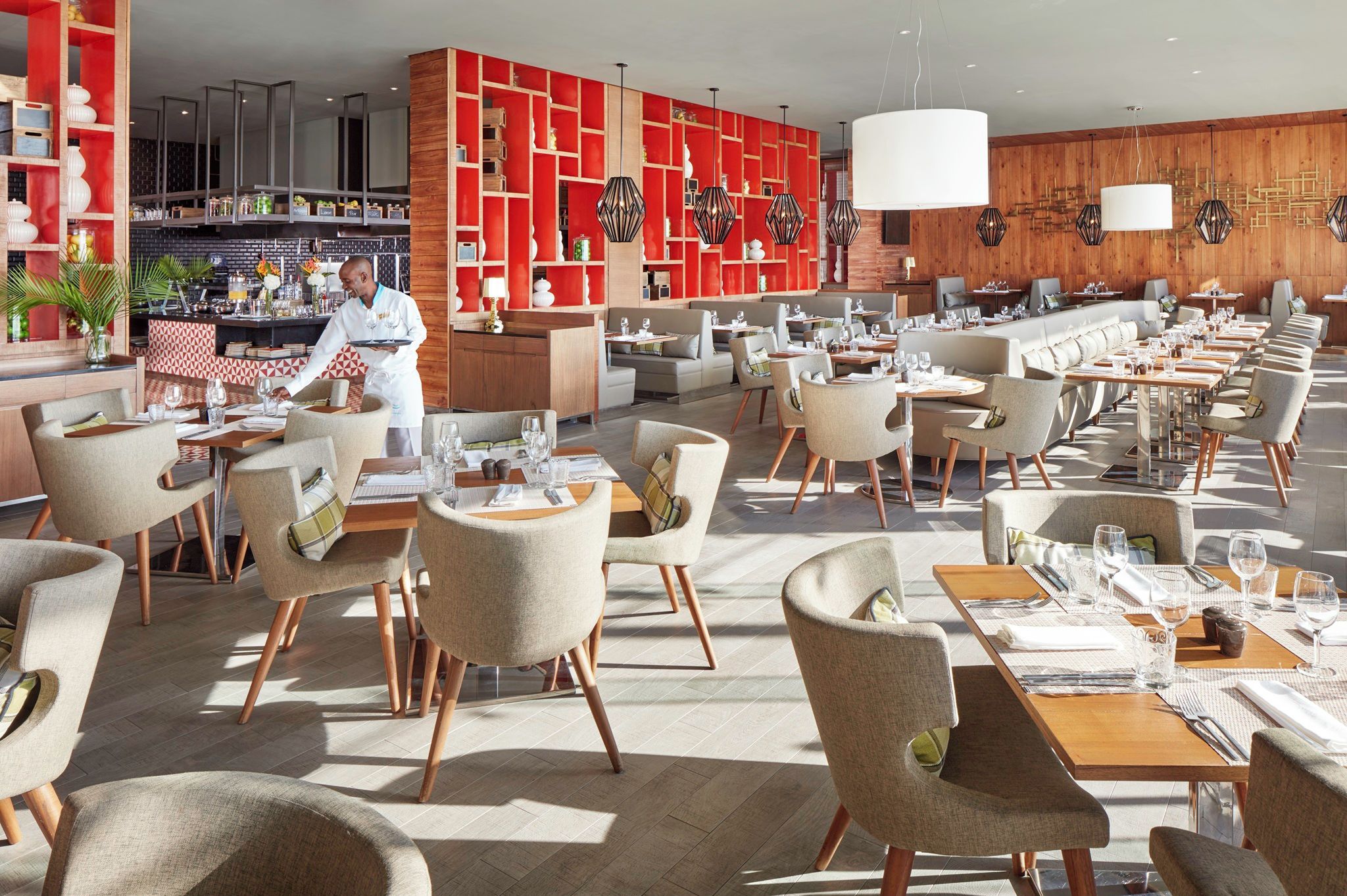 Restaurante moderno com amplo espaço para refeições, várias mesas e um bar, onde um chef está a servir.