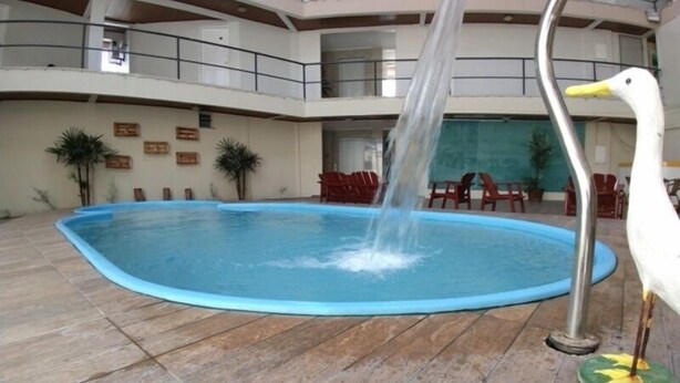 Una piscina con una fuente, rodeada por una terraza de madera y sillas rojas.