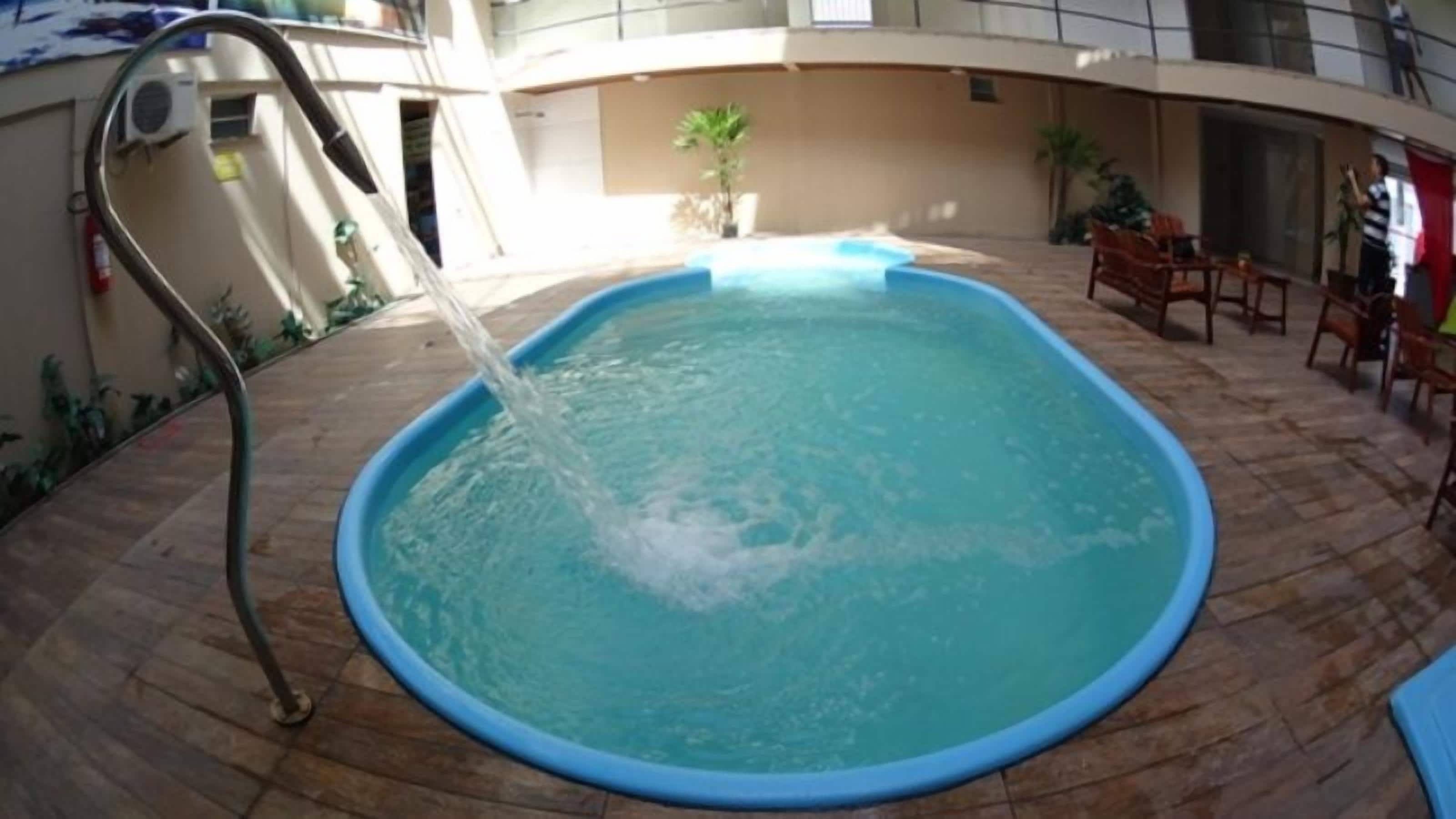 A swimming pool with a water fountain feature, surrounded by a tiled deck and outdoor furniture.