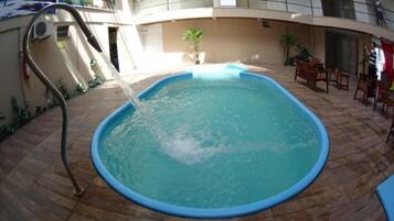 A swimming pool with a water fountain feature, surrounded by a tiled deck and outdoor furniture.