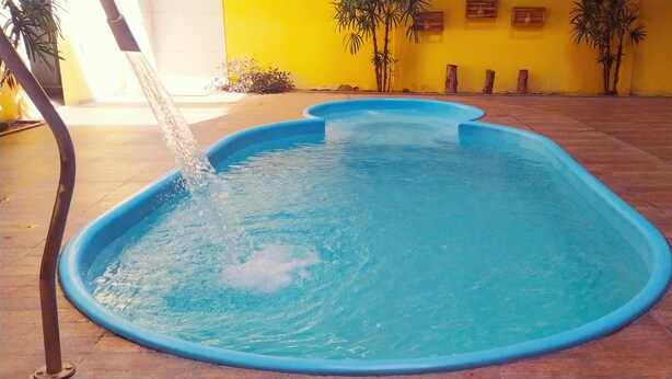 Una piscina con fuente, rodeada de un patio con baldosas y paredes amarillas.