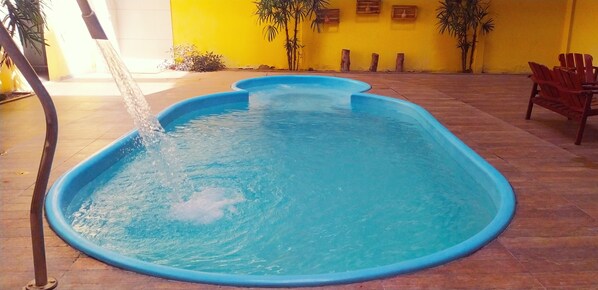 A swimming pool with a water fountain feature, surrounded by a tiled patio and yellow walls.