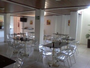 A dining area with glass tables and chairs, white walls, and a flat-screen TV mounted on the wall. - Hotel Aracaju Express (Aracaju)