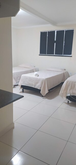 A room with two beds, a window with blinds, a tiled floor, and a small table.