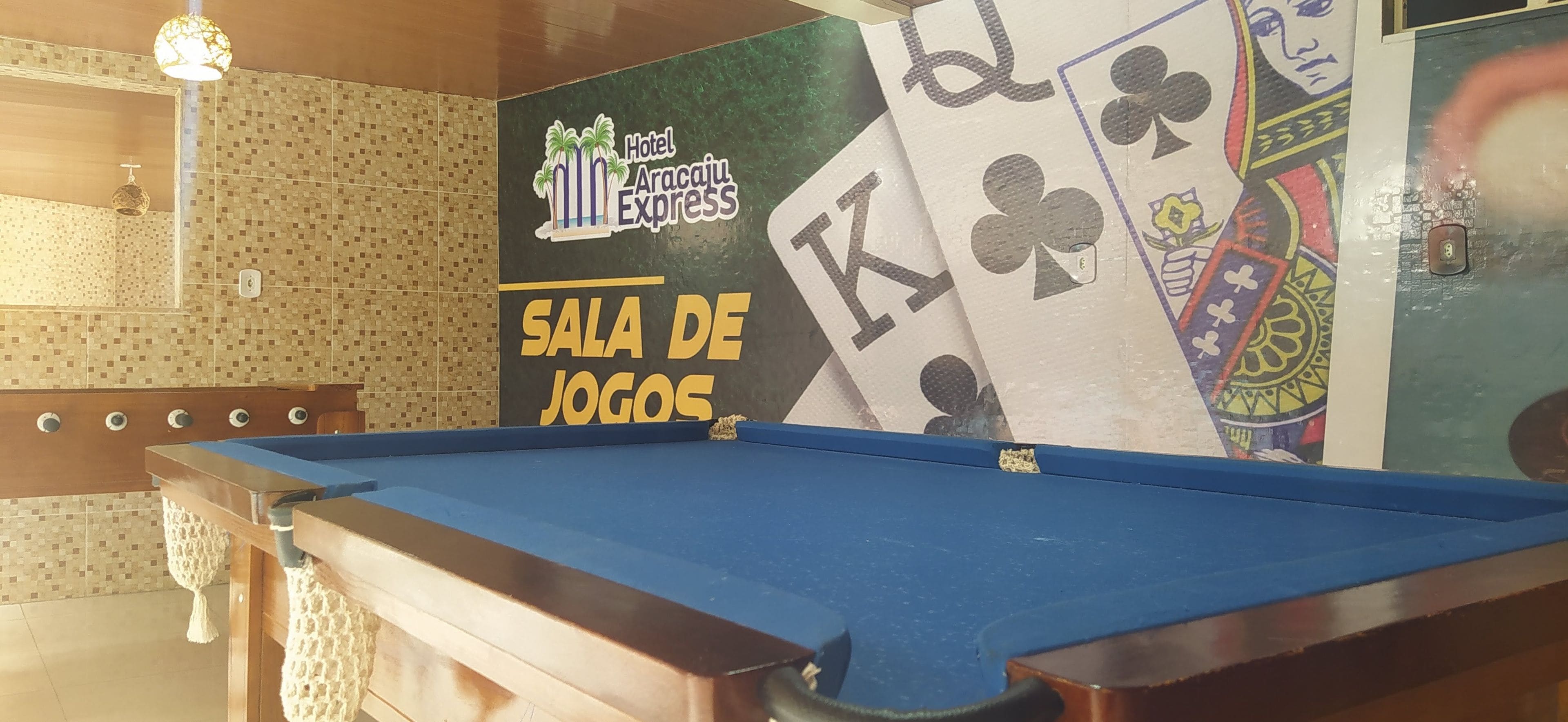 A billiards table in a room with a tiled wall and a poster advertising Hotel Aracaju Express.