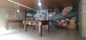 Une salle de billard équipée d’une table de billard, de deux bancs en bois et d’une fresque représentant une main jouant au billard.