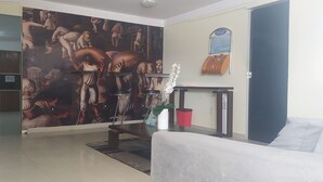 Una sala de estar con una máquina expendedora roja, un sofá blanco, un mural y una pequeña mesa con una planta en maceta.
