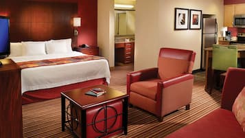 A hotel room with a bed, a desk, a chair, a kitchenette, and a bathroom.