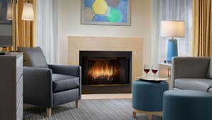 Un salon moderne avec une cheminée, deux fauteuils, des poufs, une table d’appoint avec des verres à vin et un tableau au mur.