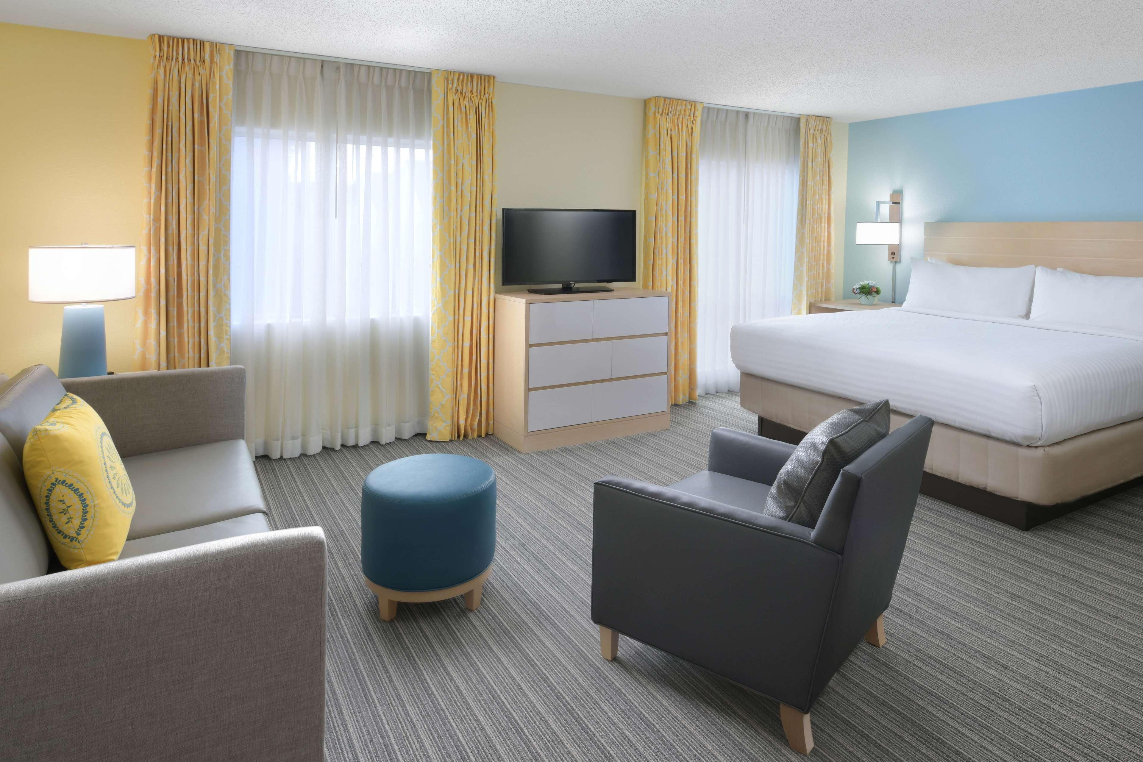 A hotel room with a bed, two armchairs, a sofa, a television on a cabinet, and a lamp.