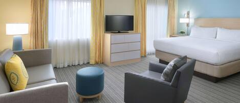 A hotel room with a bed, two armchairs, a sofa, a television on a cabinet, and a lamp.
