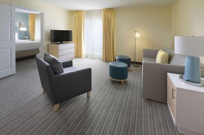 Een hotelkamer met een bed, twee banken, een televisie, een lamp en een vloerlamp.