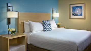 A hotel room with a bed, two bedside tables, a nightstand, a drawer, a wall-mounted lamp, and a framed picture.