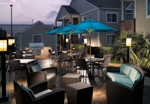 Een terras buiten met rieten meubels, tafels en blauwe parasols.