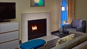 Un salon moderne doté d’une cheminée, d’un téléviseur à écran plat, d’un canapé et d’un coin repas avec une lampe et une table.