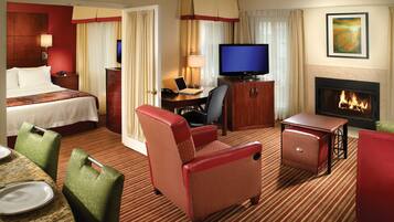 Quarto de hotel com cama, escrivaninha, televisão, lareira e área de estar.