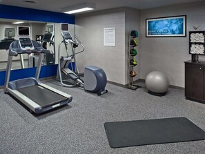 Une salle de sport équipée de tapis de course, de vélos elliptiques, d’un vélo d’appartement, d’un t éléviseur fixé au mur, d’une affiche motivante, d’un présentoir à casques et d’un grand ballon d’exercice.