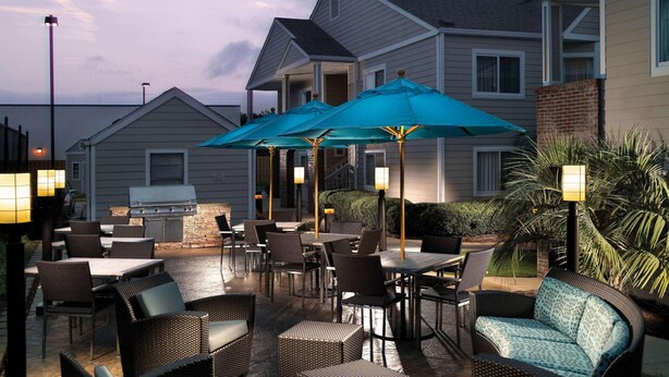 Un espace extérieur aménagé en terrasse, avec des meubles en osier, des tables et des parasols bleus.