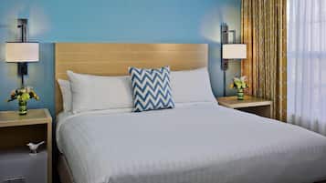 Una habitación de hotel con una cama grande, dos mesitas de noche, un cajón y una lámpara.