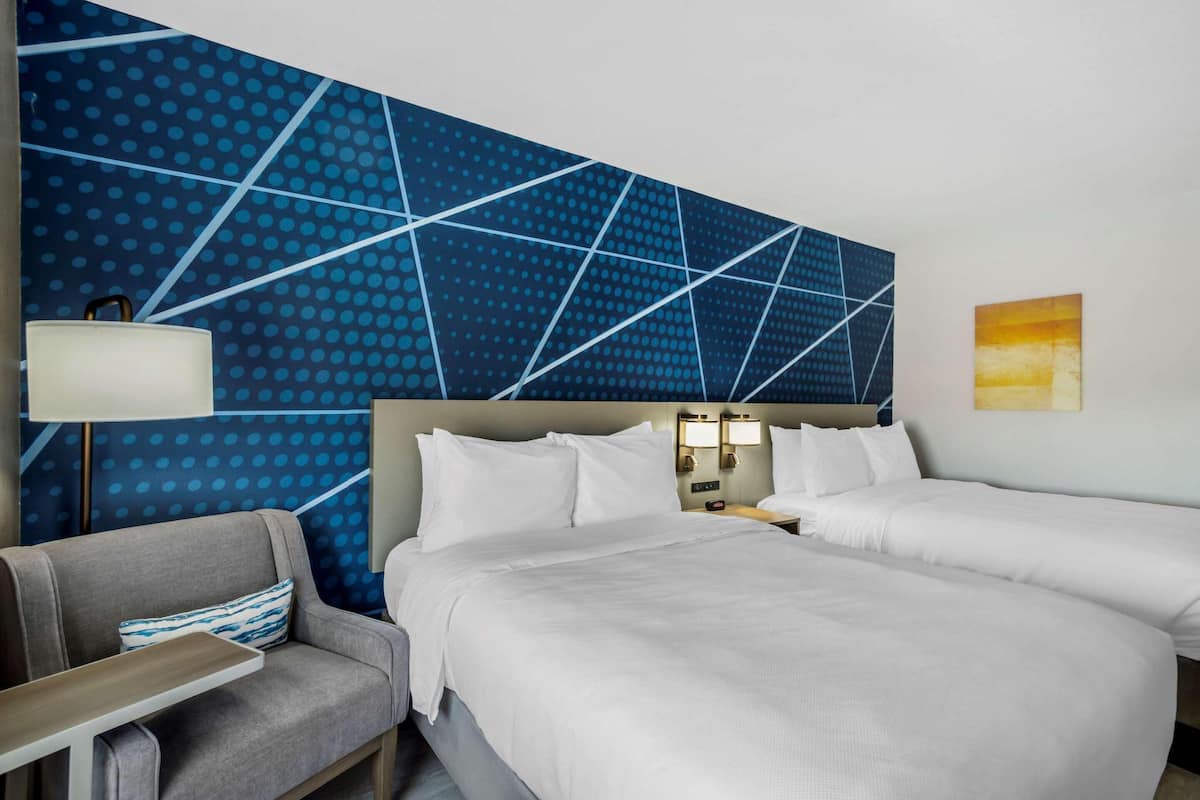 A hotel room with a large bed, two bedside tables, a sofa, and a patterned wall.