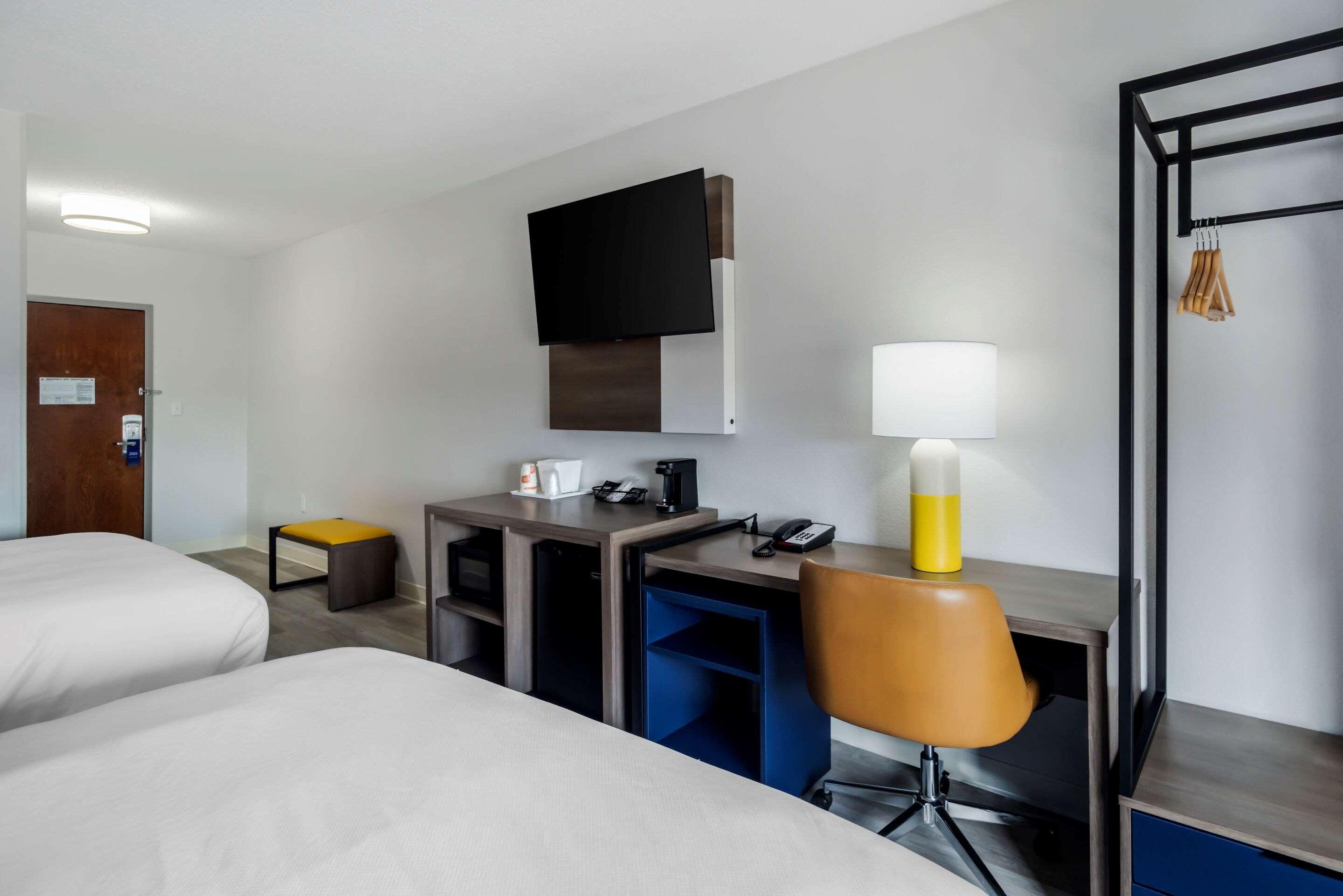 Une chambre d’hôtel avec deux lits, un bureau, une chaise, un téléviseur fixé au mur et une lampe.