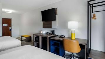 Une chambre d’hôtel avec deux lits, un bureau, une chaise, un téléviseur fixé au mur et une lampe.