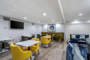 A modern room with yellow chairs and tables, a blue sofa, and a large painting on the wall. - Comfort Inn & Suites Lexington South (Lexington)