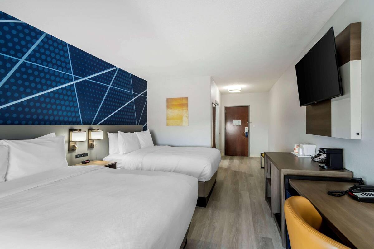 A hotel room with two beds, a desk, a chair, a TV, and a bathroom door.