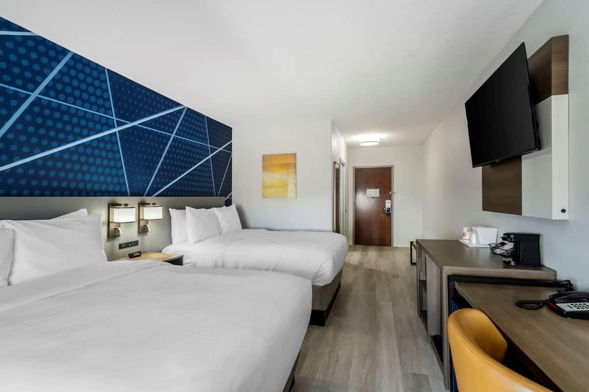 A hotel room with two beds, a desk, a chair, a TV, and a bathroom door.