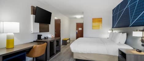Una habitación de hotel con cama, escritorio, silla y televisor montado en la pared.