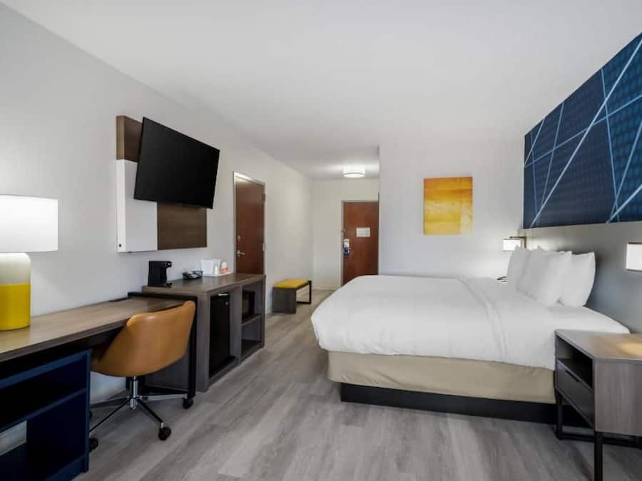 A hotel room with a bed, desk, chair, and a TV mounted on the wall.