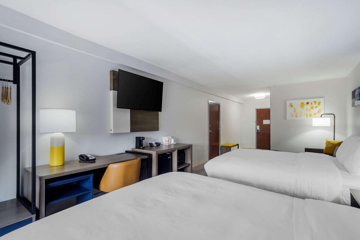A hotel room with two beds, a desk with a chair, a TV, a coffee maker, and a lamp.