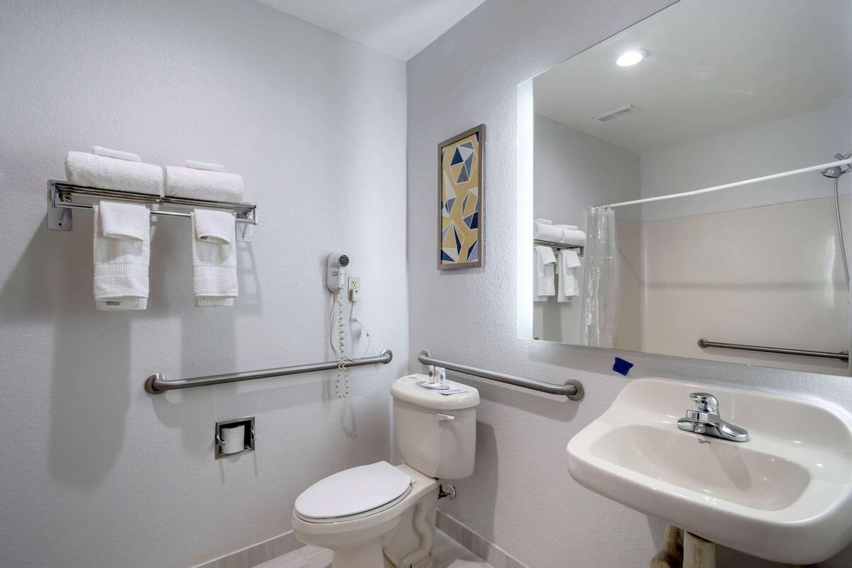 A bathroom with a toilet, a sink, a towel rack with towels, a hand dryer, and a mirror.