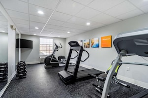 Un gimnasio con cintas de correr, mancuernas y un espejo grande.