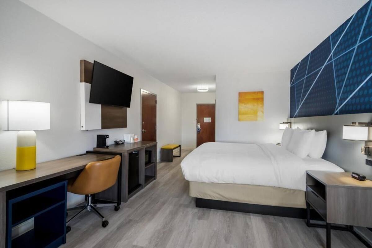 A hotel room with a bed, desk, chair, and a TV mounted on the wall.