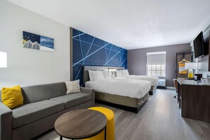 Moderni hotellihuone, jossa on sänky, sohva, pyöreä pöytä ja työpöytä tuolilla.