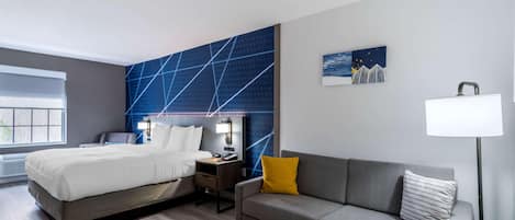 Ein modernes Hotelzimmer mit Bett, einer Couch, einem kleinen Tisch, einem Nachttisch, einer Lampe und einem Fenster.