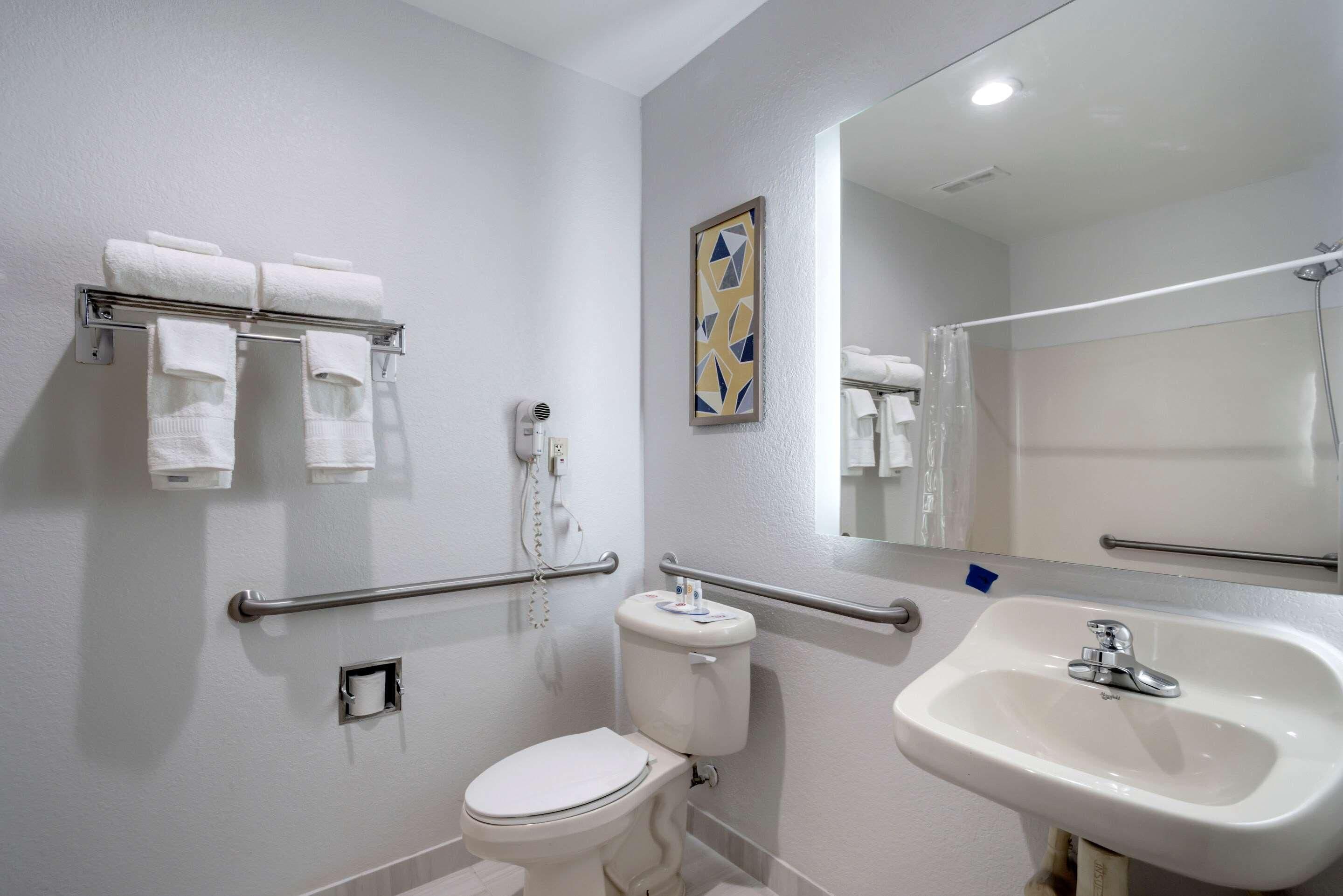Un baño con inodoro, lavamanos, toallero con toallas, secador de manos y espejo.
