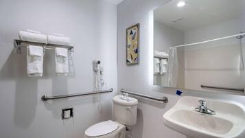 Un baño con inodoro, lavamanos, toallero con toallas, secador de manos y espejo.
