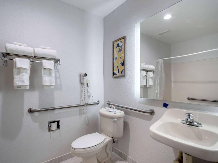 Un baño con inodoro, lavamanos, toallero con toallas, secador de manos y espejo.