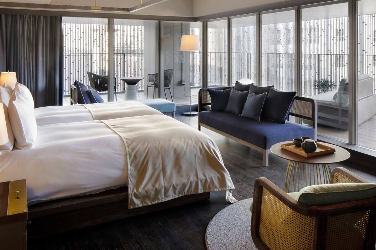 A hotel room with a large bed, a sofa, a small table with a tray, and a chair.