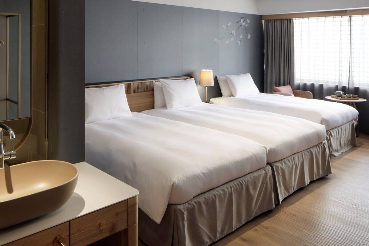 Une chambre d’hôtel avec deux lits, un grand lavabo, un miroir, une petite table avec une lampe et une chaise.