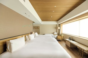 Une chambre d’hôtel avec un grand lit, un bureau avec un ordinateur portable, une chaise et une fenêtre avec des stores.