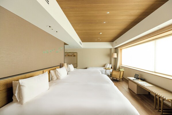 A hotel room with a large bed, a desk with a laptop, a chair, and a window with blinds.