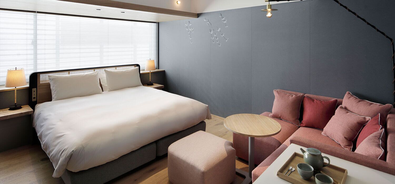 Et moderne hotelværelse med en stor seng, en sofa, et lille bord og et vindue med persienner.