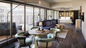 A modern hotel room with a large bed, a sofa, a dining table with chairs, and a view through large windows. - Good Nature Hotel Kyoto (Kyoto)