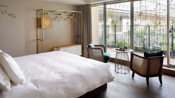 Une chambre d’hôtel avec un grand lit, une armoire avec un porte-manteau, une petite table avec un plateau, et un balcon agrémenté de plantes.
