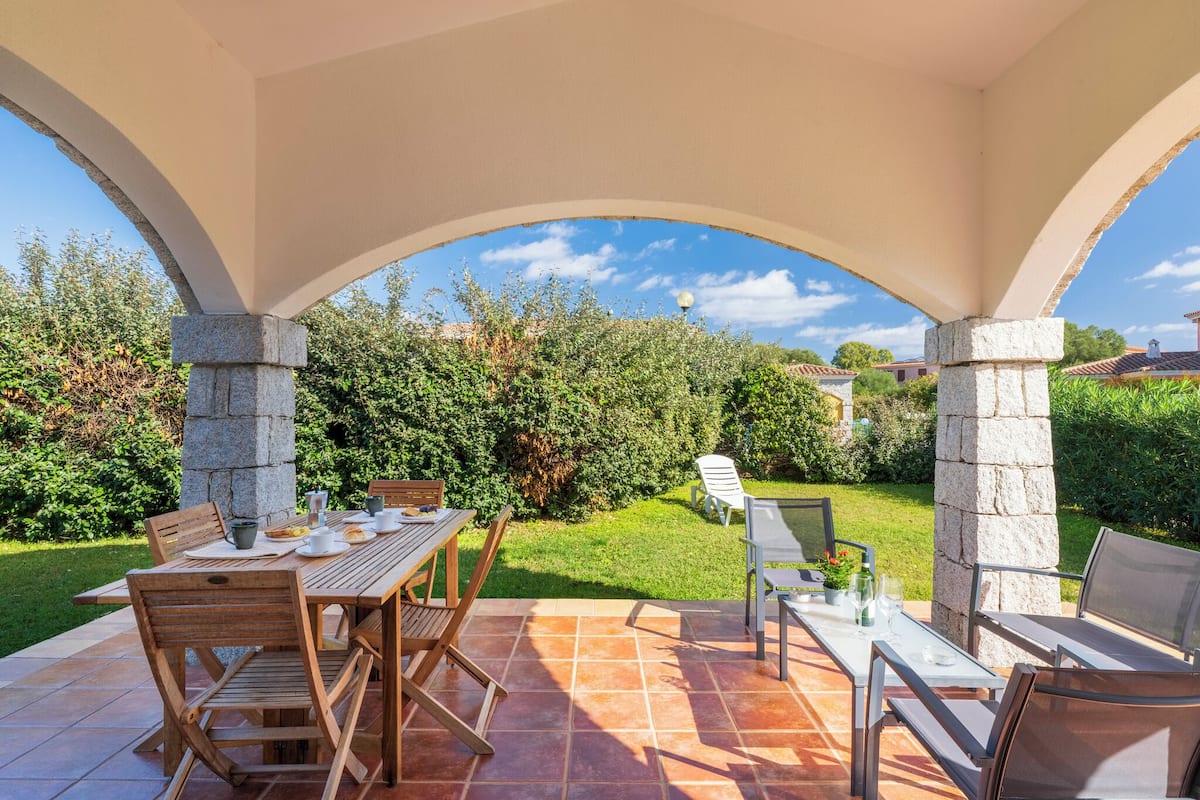 Une terrasse extérieure avec une table et des chaises, des piliers en pierre et une vue sur un jardin.